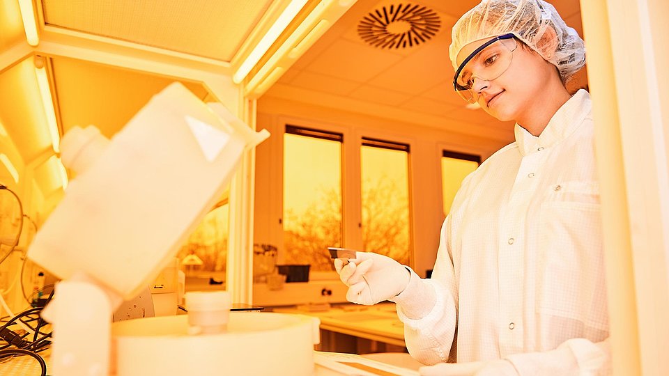 A young woman in protective clothing places a wafer piece in a coating spinner