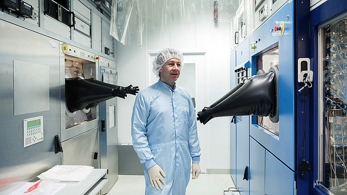 A worker in laboratory clothes in front of an epitaxial reactor with black rubber gloves attached.