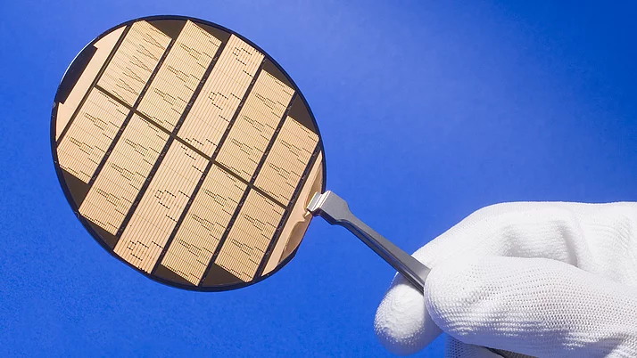 Ein Handgriff hält eine kreisförmige Halbleiterwaferplatte, die mit schmalen, parallelen Streifen in verschiedenen Mustern graviert ist.