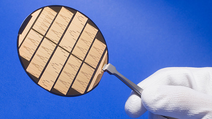Ein Handgriff hält eine kreisförmige Halbleiterwaferplatte, die mit schmalen, parallelen Streifen in verschiedenen Mustern graviert ist.
