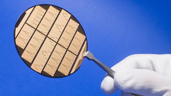 A handle holds a circular semiconductor wafer plate engraved with narrow, parallel stripes in various patterns.