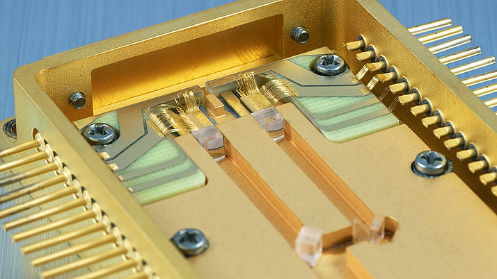 Close-up of a golden microchip with conductive tracks and fine wires. The chip is integrated into a housing that shows metallic and transparent elements.