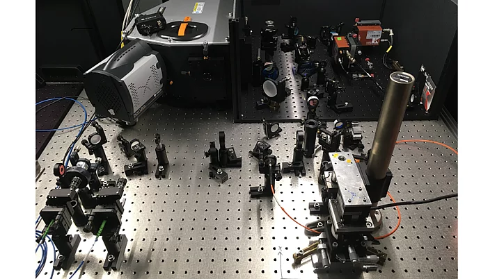 Scientific apparatus on a perforated metal plate. Various optical instruments, holders and cables are distributed.