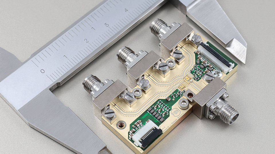 Close-up view of a circuit board featuring multiple metal connectors and electronic components, measured with a caliper. The board includes green circuitry and gold traces.