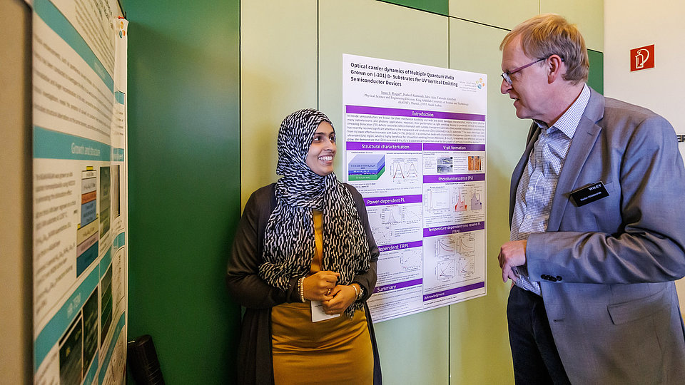 Frau stellt einem Mann ihr wissenschaftliches Poster vor.