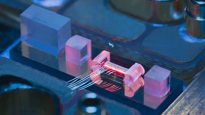 Close-up of a microelectronic circuit with several transparent elements. A glowing red wire is visible between two glass blocks.