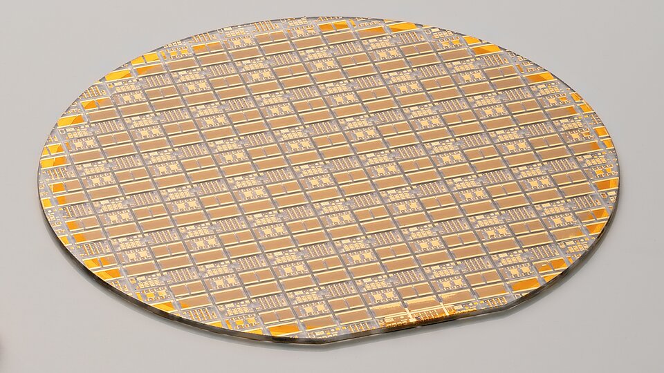 Gallium oxide wafer with lateral transistors. The surface of the round wafer is covered with various geometric shapes in shades of gold and brown.