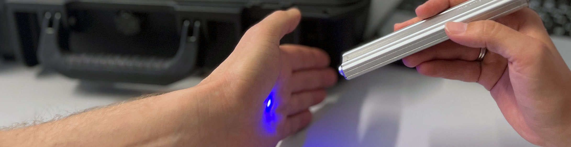A palm is scanned with the Raman system sensor. The Raman system (a suitcase and a laptop) can be seen in the background.
