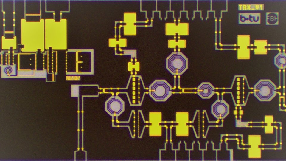 Close-up view of a fabricated compact digital transceiver (TRx) MMIC. The integrated circuit includes a low-noise amplifier with integrated switch (LNAiS) and a digital power amplifier (PA). The rectangular chip has intricate circuitry visible on its surface.