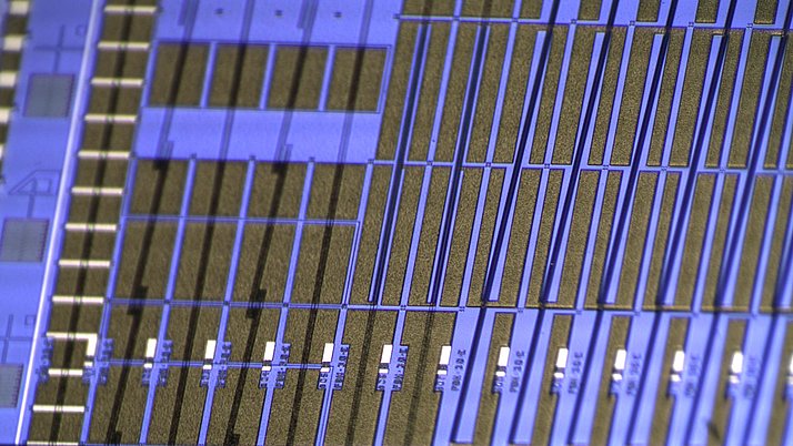 Mikroskopische Aufnahme von einer Leiterplatte mit feinen, parallelen Strukturen in blau und gold. 