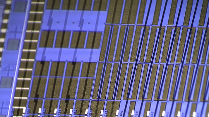 Microscopic image of a printed circuit board with fine, parallel structures in blue and gold.