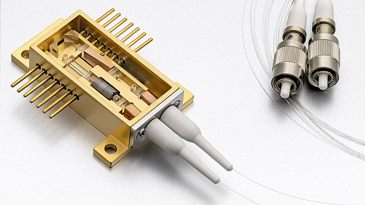 The picture shows an open amplifier and frequency converter module. Inside is a microisolator, a semiconductor amplifier and a non-linear crystal for frequency doubling. Two glass fibers with metallic connectors can be seen on the right. The lower one is the fiber input, the upper one the fiber output.
