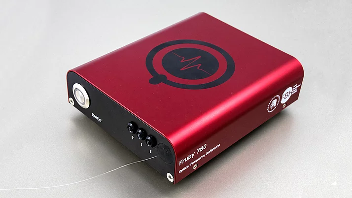 A red module with a glossy surface and a large black logo on the top. There are switches and connections on the front.