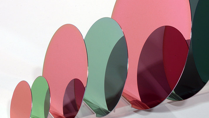 A series of partially transparent, colorful, oval wafers in green, pink and red, which are arranged and overlap. 