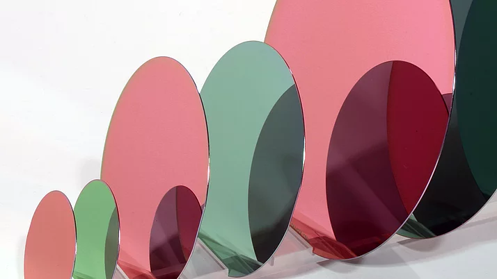 A series of partially transparent, colorful, oval wafers in green, pink and red, which are arranged and overlap. 