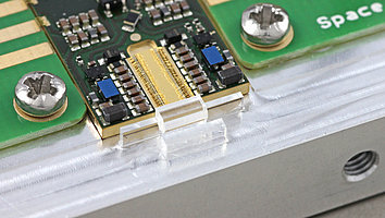 Die Abbildung (Detailaufnahme eines Nanosekunden-Lasermoduls für LiDAR-Anwendungen) zeigt im Zentrum eine goldene Laserdiode mit Drähten sowie eine elektronische Platine mit verschiedenen Bauteilen, einschließlich Widerständen und integrierten Schaltungen. Einige Schrauben sind sichtbar, die die Montage sichern.