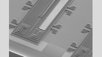 Rasterelektronenmikroskop-Aufnahme eines GaAs-basierten Verstärker-Chiplets mit feinen, µm-großen Strukturen. Zu sehen sind Wellenleiter-, Anker- und Kontaktstrukturen auf der Oberfläche des Chips.
