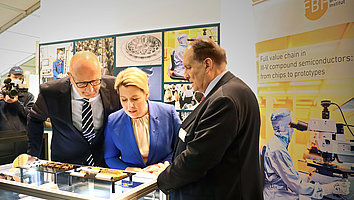 Dietmar Woidke and Franziska Giffey bend over laser modules for space applications during the press tour at the ILA 2022. FBH Director Günther Tränkle explains their function.
