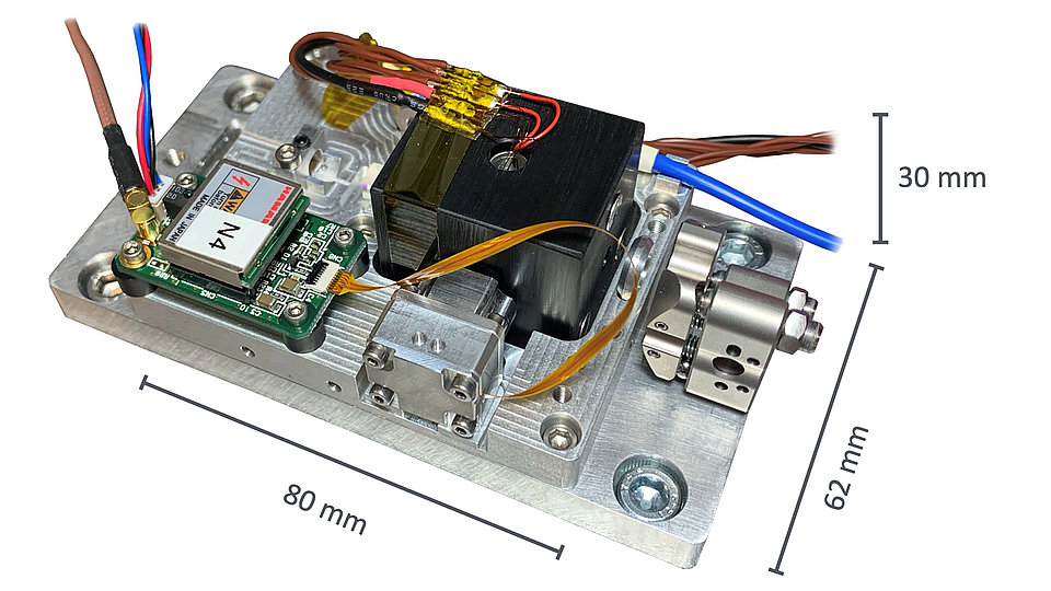 Photo of a prototype of the miniaturized rubidium two-photon optical frequency reference. The prototype is mounted on a metallic base plate and has dimensions of approximately 80 mm in length, 62 mm in width, and 30 mm in height.