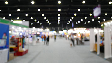 Blick in eine Messehalle: Ein Gang mit einigen Menschen. Links und rechts sind Messestände zu sehen.
