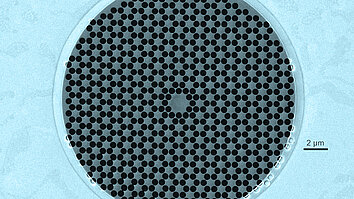 A circular arrangement of small black dots on a light blue background, representing a microscopic pattern. The dots are evenly spaced, creating a textured appearance. A scale bar in the image indicates a measurement of 2 micrometers.