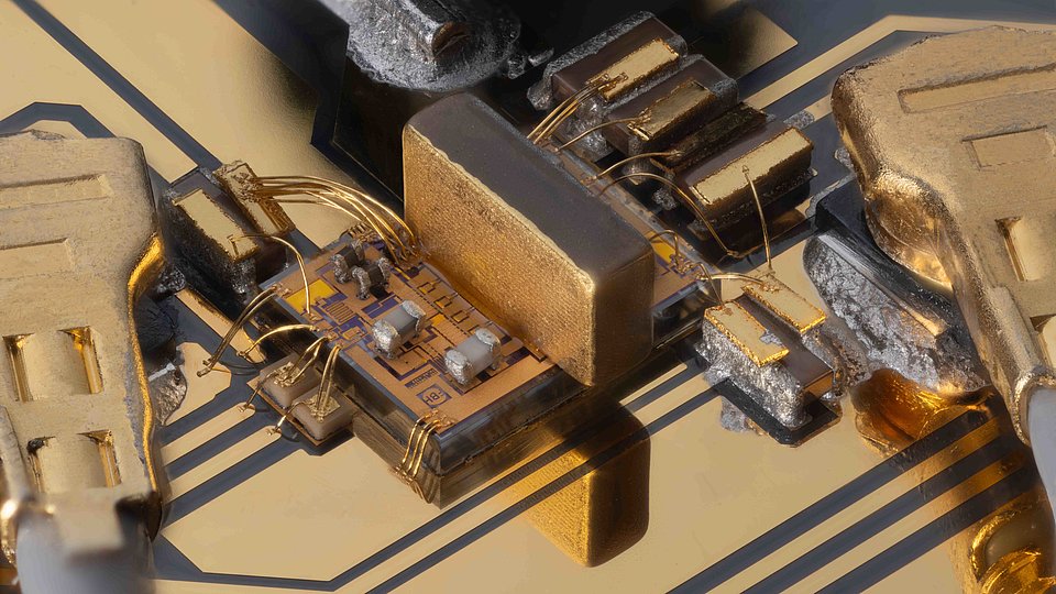 Close-up of an electronic circuit on a printed circuit board. Several golden components can be seen, including a rectangular chip and several small components with wire connections.