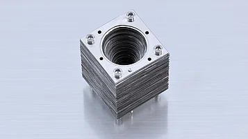 Photograph of an assembled corrugated horn made from stacked square metal plates fastened with four screws, with a tapered circular opening at the center.