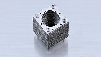 Photograph of an assembled corrugated horn made from stacked square metal plates fastened with four screws, with a tapered circular opening at the center.