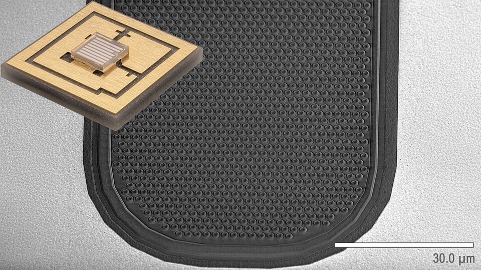 Das Bild zeigt einen mikrogefertigten Bauteil auf einer strukturierten, schwarzen Oberfläche. Der Bauteil hat eine quadratische Form mit einem dünnen, rechteckigen Element in der Mitte. Es sind Maße in Mikrometern angegeben, um die Detailgenauigkeit zu verdeutlichen.