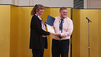 Programmchair Paul O. Leisher (rechts) überreicht Andrea Knigge vom FBH (links) die Urkunde "Big Laser Award"