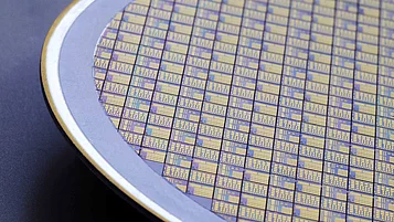 Silicon wafer covered with a pattern of intricate, colorful designs. The wafer is partially visible, with a metallic edge surrounding it.