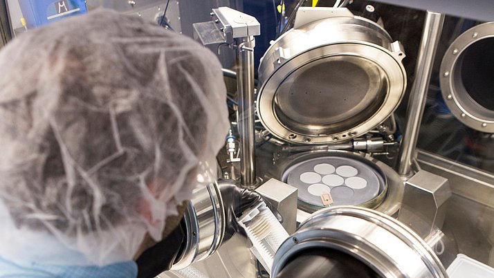 Ein Mitarbeiter in Schutzkleidung arbeitet an einer wissenschaftlichen Maschine. In der Maschine befinden sich mehrere runde Objekte, die sorgfältig platziert werden.