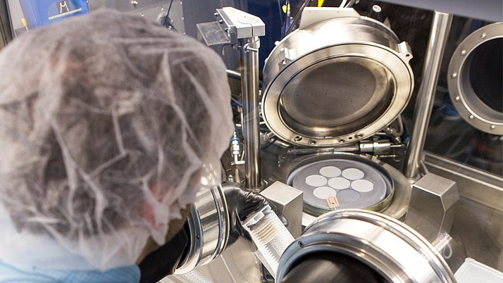 Ein Mitarbeiter in Schutzkleidung arbeitet an einer wissenschaftlichen Maschine. In der Maschine befinden sich mehrere runde Objekte, die sorgfältig platziert werden.