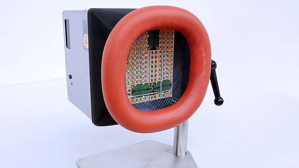 UV-Bestrahlungssystem zur Hautdesinfektion mit silbernem Gehäuse, großer roter, gepolsterter Ringöffnung an der Vorderseite und einer Anordnung von UV-LEDs, montiert auf einem Metallständer mit seitlichem Verstellhebel, um das System zu schwenken.