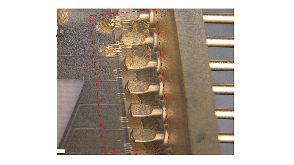Nahaufnahme eines elektronischen Bauteils, das zahlreiche kleine, goldene Kontaktstifte zeigt. Die Stifte sind in einer Reihe angeordnet und teilweise mit feinen Drähten verbunden.