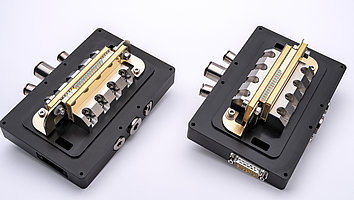 2 Diodenlaser-Module, die nebeneinander liegen. Beide Module sind auf einem schwarzen Kunststoffblock aufgebaut, der als Kühlung der Doppelemitter-Diodenlaser dient. In der Mitte der Module sieht man die vertikal aufgebauten Emitter und die darauf platzierten Linsen.
