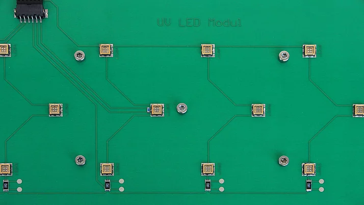 Eine grüne Leiterplatte mit mehreren UV-LED-Modulen. Die Module sind gleichmäßig verteilt und durch dünne leitende Bahnen miteinander verbunden.
