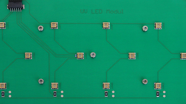 Eine grüne Leiterplatte mit mehreren UV-LED-Modulen. Die Module sind gleichmäßig verteilt und durch dünne leitende Bahnen miteinander verbunden.