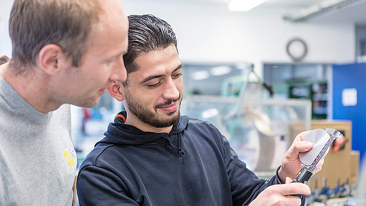 One industrial mechanic measures a component, another watches.