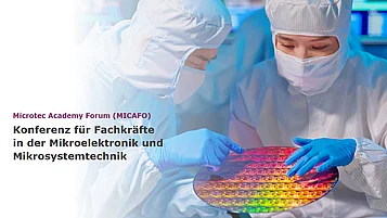 Two specialists in protective clothing examine a wafer together under a work lamp.