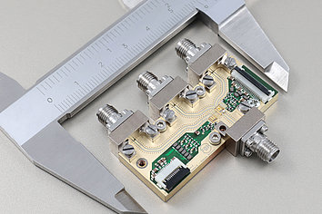 Close-up view of a circuit board with multiple metallic connectors. A caliper measures the distance between components. The board features intricate pathways and various electronic elements, indicating its use in a technical application.