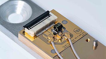 Buck converter on a circuit board. Filigree wires, connections and golden circuits can be seen. A surrounding metal housing with fixing screw is also visible.
