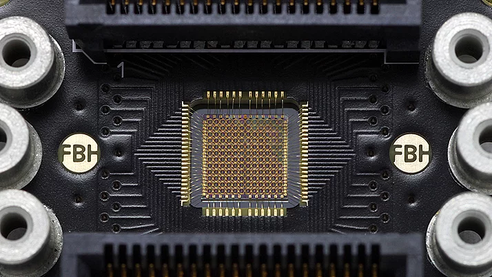 Circuit board featuring a central microchip surrounded by multiple connection ports. The microchip has a grid of small pins and is flanked by solder points and labeled areas.