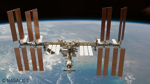Die Internationale Raumstation ISS im Weltraum, dahinter ein Teil der Erde.