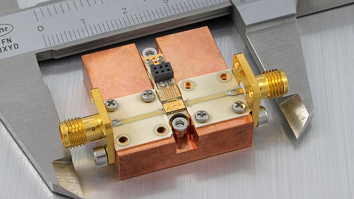 Ein Messschieber liegt neben einem montierten elektronischen Bauteil, das hauptsächlich aus Kupfer und Platine besteht. Das Bauteil hat zwei goldene Anschlüsse an den Seiten und eine zentrale Schaltung, die mit kleinen Schrauben befestigt ist.