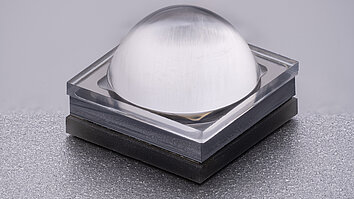 Close-up of a square LED with a transparent, dome-shaped lens on a dark base.