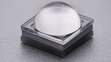 Close-up of a square LED with a transparent, dome-shaped lens on a dark base.