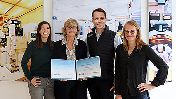 Die Preisträger des IEEE Technical Skills Educator Award stehen vor einer Wand mit Bildern aus dem Reinraum und halten die Urkunde in der Hand. Von links nach rechts: Sabine Harms, Uta Voigt, Jens Hofmann, Anja Quednau.