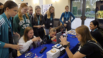 An einem Infostand stehen mehrere Mädchen und informieren sich über Berufe im Hightech-Bereich. Sie experimentieren und unterhalten sich mit den Ausstellerinnen des Ausbildungsnetzwerks ANH Berlin und einer Auszubildenden aus dem Ferdinand-Braun-Institut.