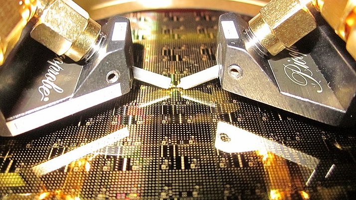 Zwei präzise Geräte, die über einer metallischen Oberfläche positioniert sind. Diese Oberfläche ist mit feinen, komplexen Mustern bedeckt.
